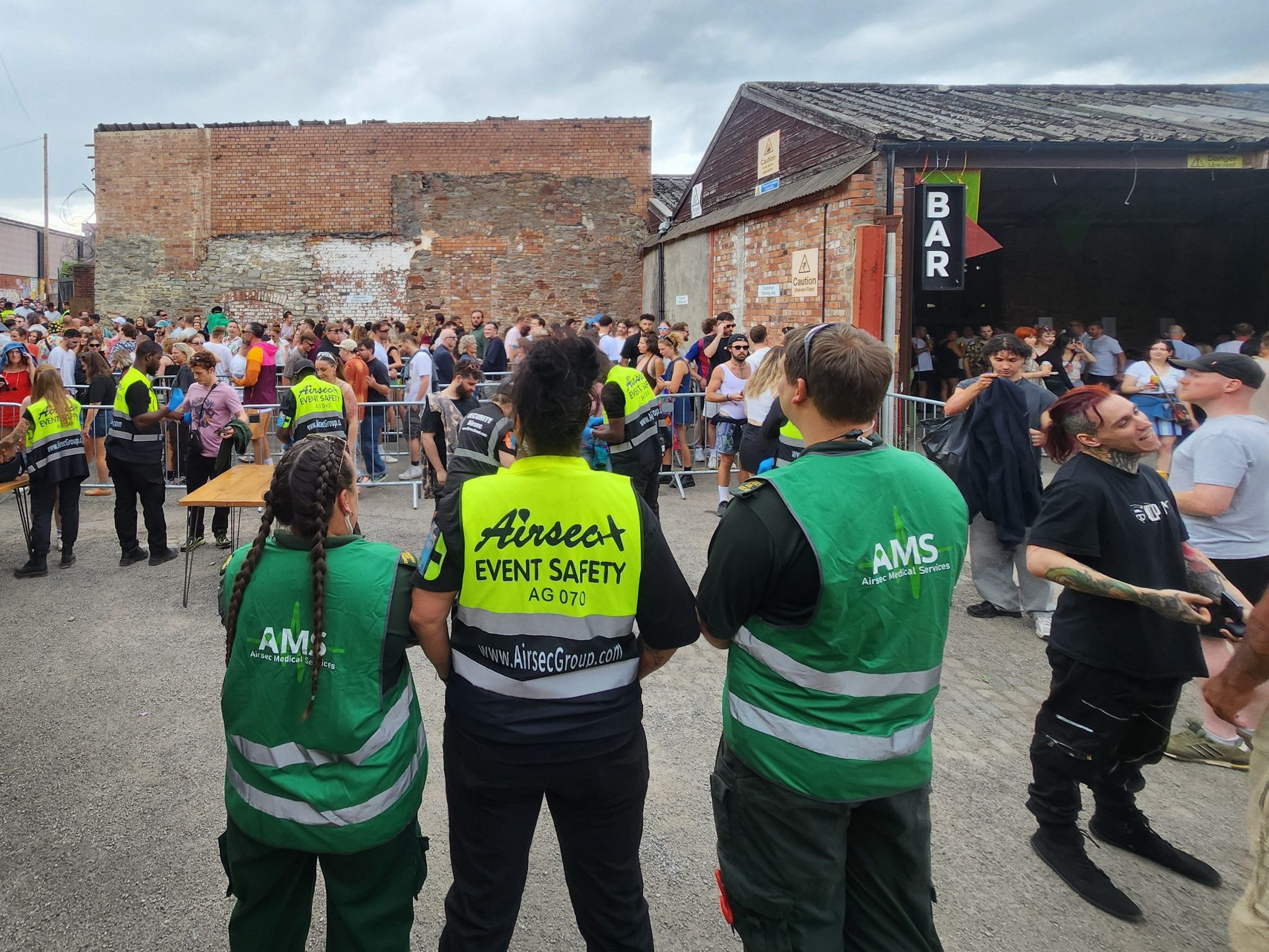 Security personnel monitoring a large crowd at an outdoor event with a bar in the background.